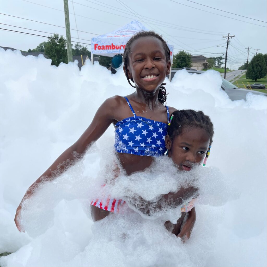 Two sisters happily playing in a pile of white foam in Washington DC, laughing and enjoying the fun atmosphere at a foam party.