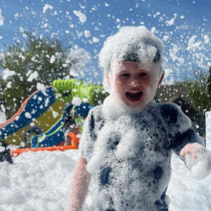 A boy smiling and enjoying foam bubbles during a foam party in Washington DC, Maryland, and Virginia.